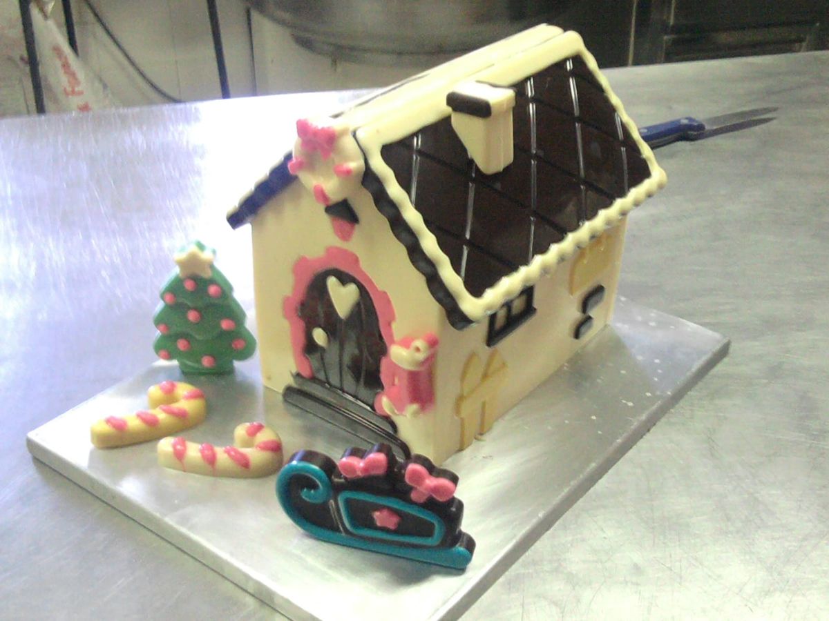 Casita de chocolate blanco y negro con un árbol y un trineo de azúcar