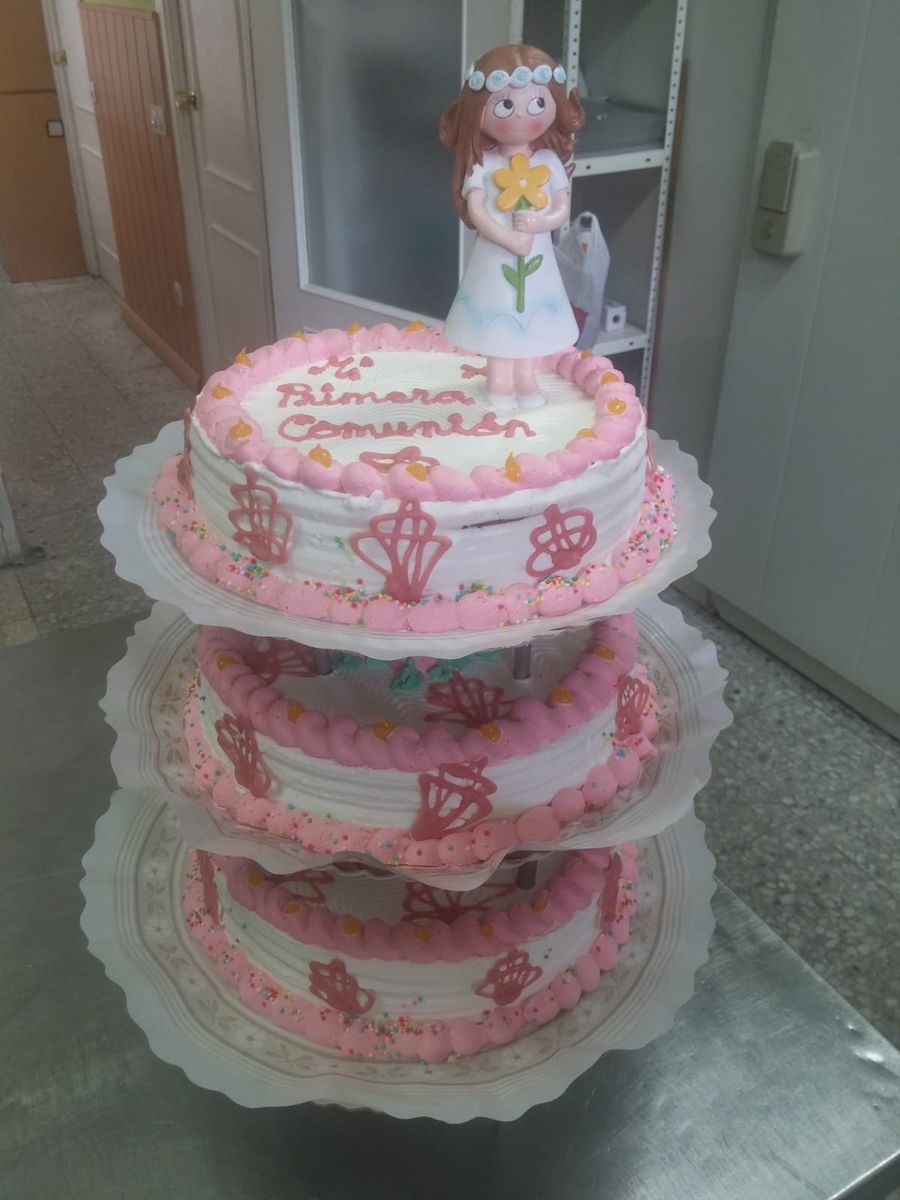Tarta de comunión de tres pisos con figura de una niña en lo alto